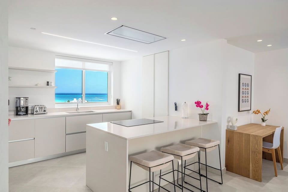 Wake up to breathtaking ocean views from your modern kitchen, where sleek white cabinetry and a chic breakfast island meet the sparkling blue sea beyond your window.