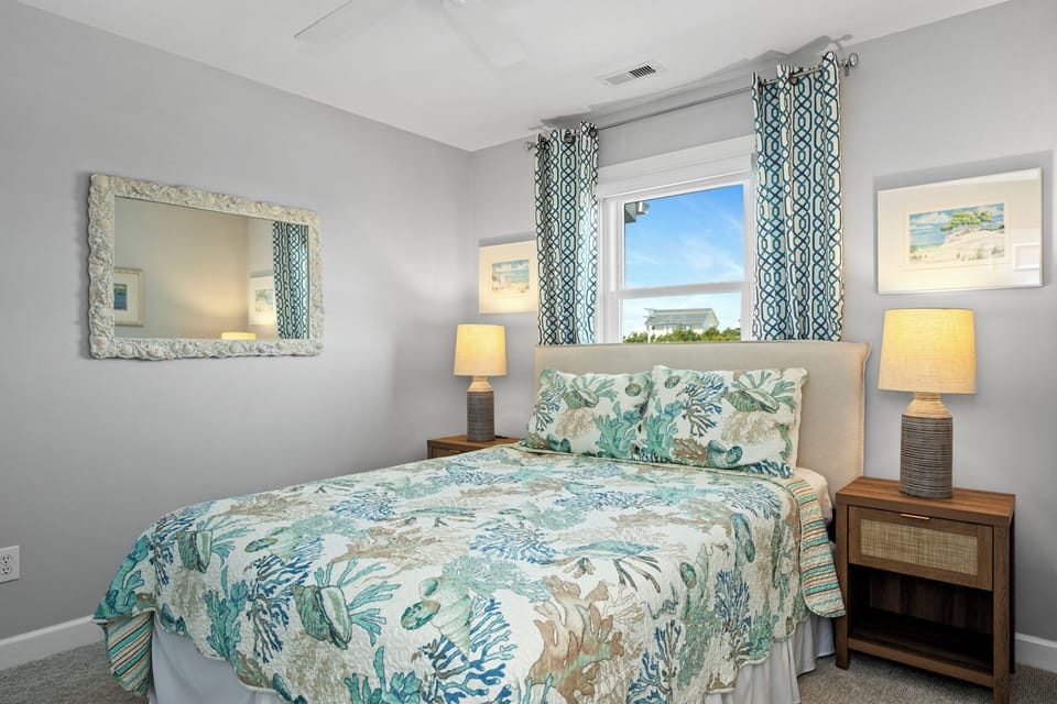 Relax in your coastal-themed bedroom featuring tropical bedding, warm lighting, and a peaceful view through elegant patterned curtains.
