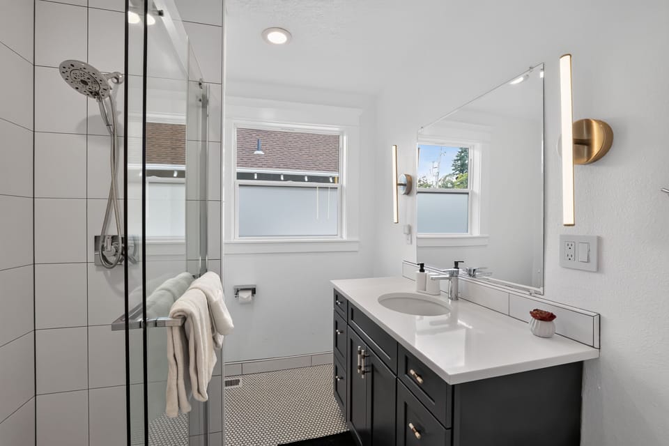 Bathroom featuring a dark vanity, modern sconces, and a glass-enclosed shower.