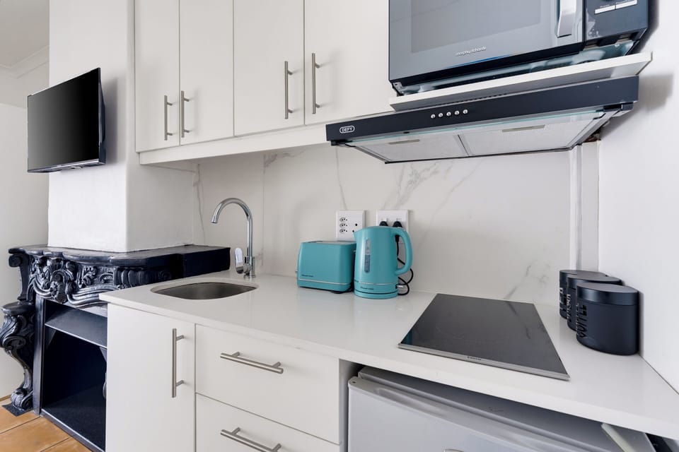 Bright modern kitchenette with cooktop, microwave, TV, and stylish touches