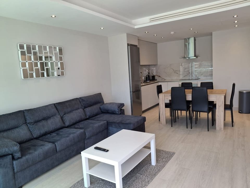 Seamless open-plan living at Marina Club. This modern layout connects our gourmet kitchen, 6-seater dining area, and plush sofa, creating a bright, social hub perfect for families or groups visiting Gibraltar.