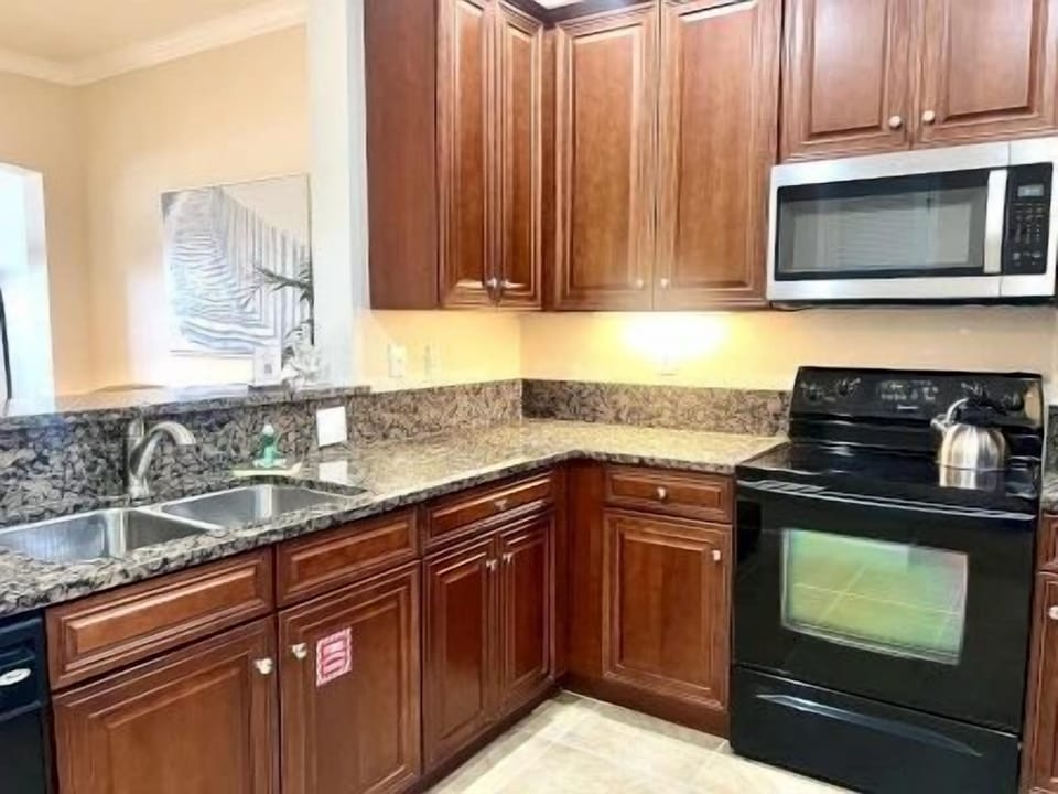 Kitchen with dark wood cabinets, granite countertops, double sinks, and a black stove