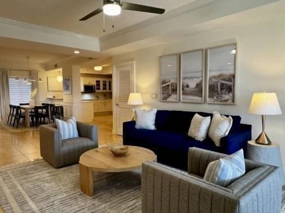 Living area with navy blue sofa, ceiling fan overhead, and natural light from the balcony windows