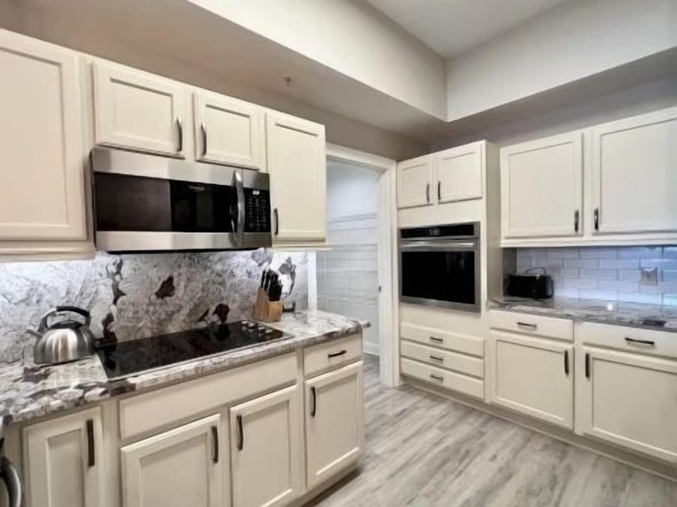 Kitchen showing double oven, granite countertops, and beige cabinetry with a white tiled backsplash