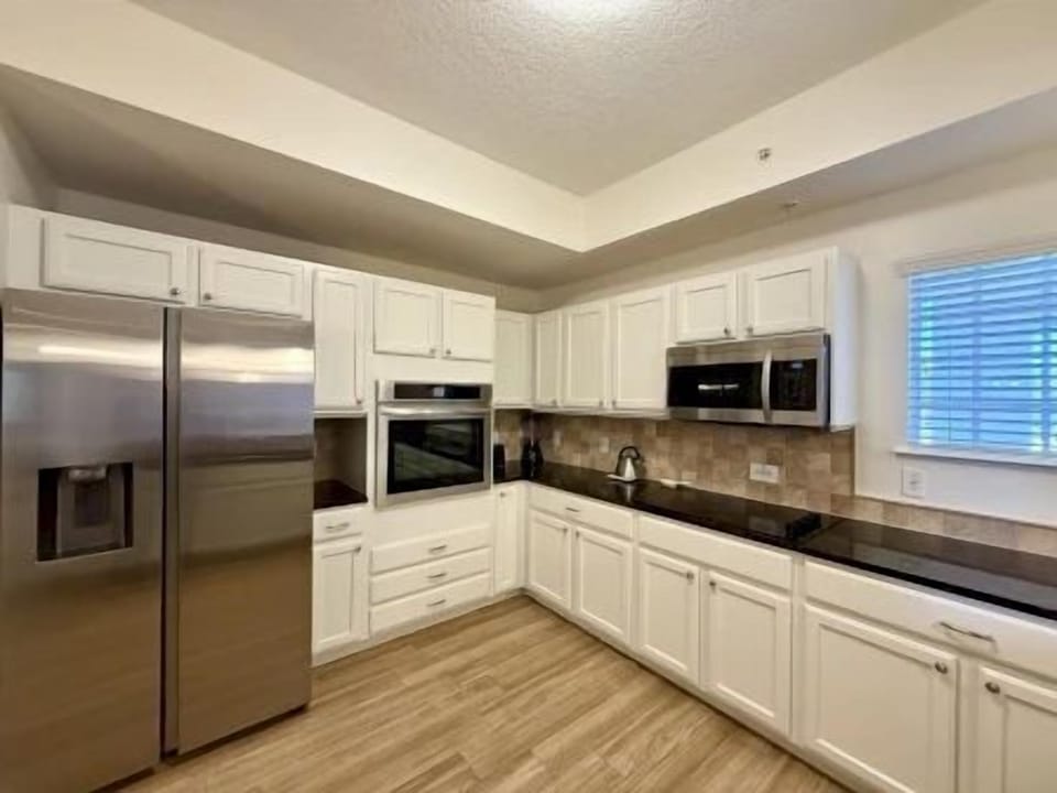 Kitchen with white cabinetry, black countertops, and stainless steel fridge and microwave