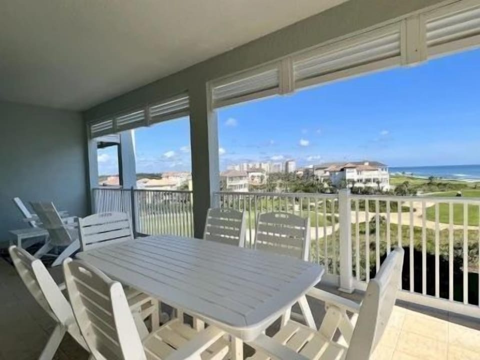 Balcony dining area with white outdoor furniture and views of the lawn and ocean beyond