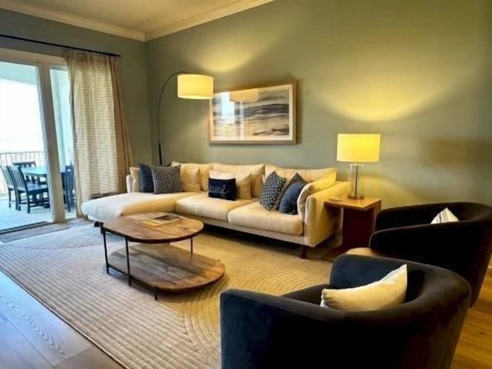 Living area with plush sectional, natural light, and open flow to the kitchen and balcony