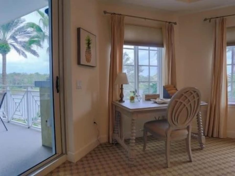 Office nook with a light desk, chair, and large window overlooking palm trees outside