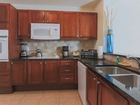 Kitchen with honey-toned wood cabinets, dark countertops, a textured backsplash, and double sink
