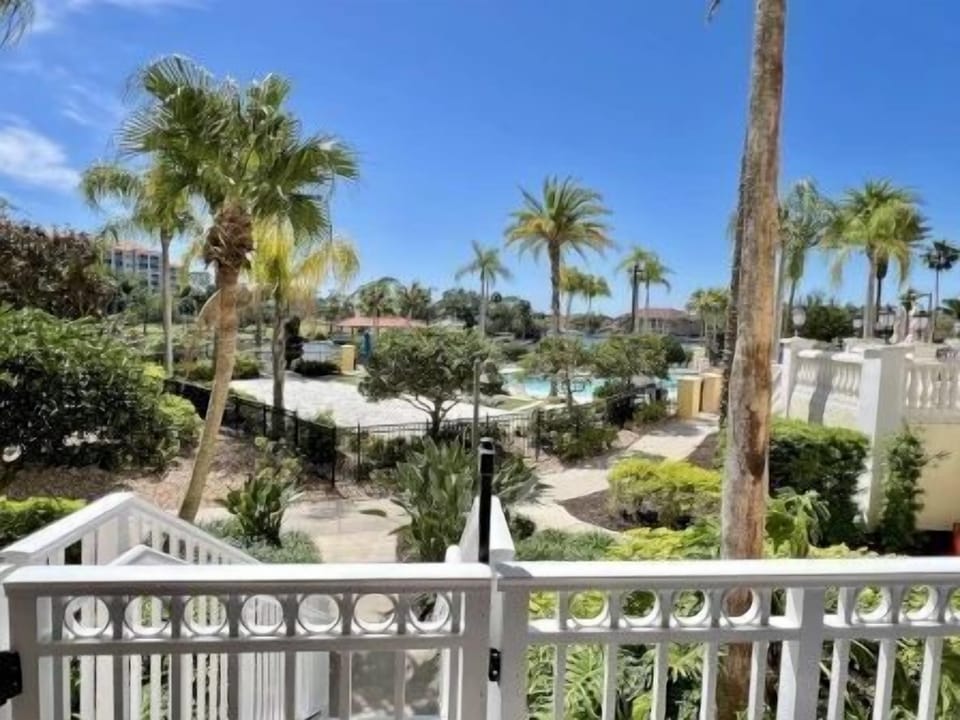 Balcony view of the pool, manicured gardens, and palm trees on a clear Florida day