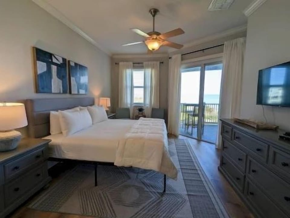 King master bedroom with white linens, ocean-view balcony access, and morning light through the window