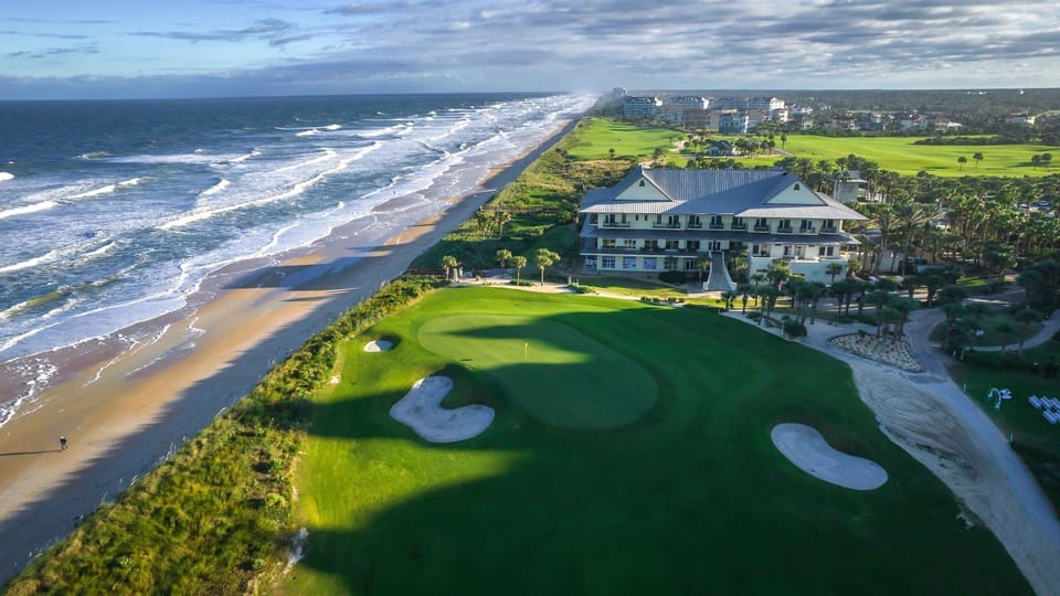 Aerial view of the golf course meeting the sandy beach at the water's edge, part of the resort amenities at Hammock Beach. 