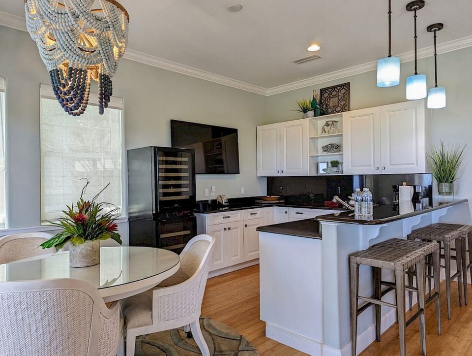 Kitchen and dining nook with round glass table, rattan chairs, bead chandelier, and bar stools