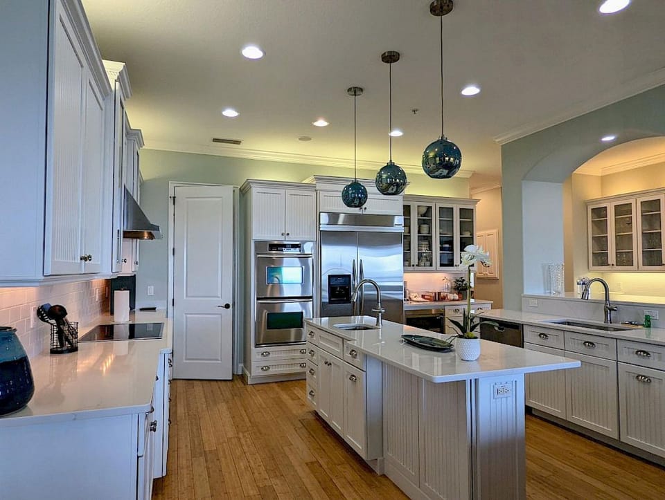 Kitchen with white beadboard cabinetry, white quartz counters, blue pendant lights, and island sink