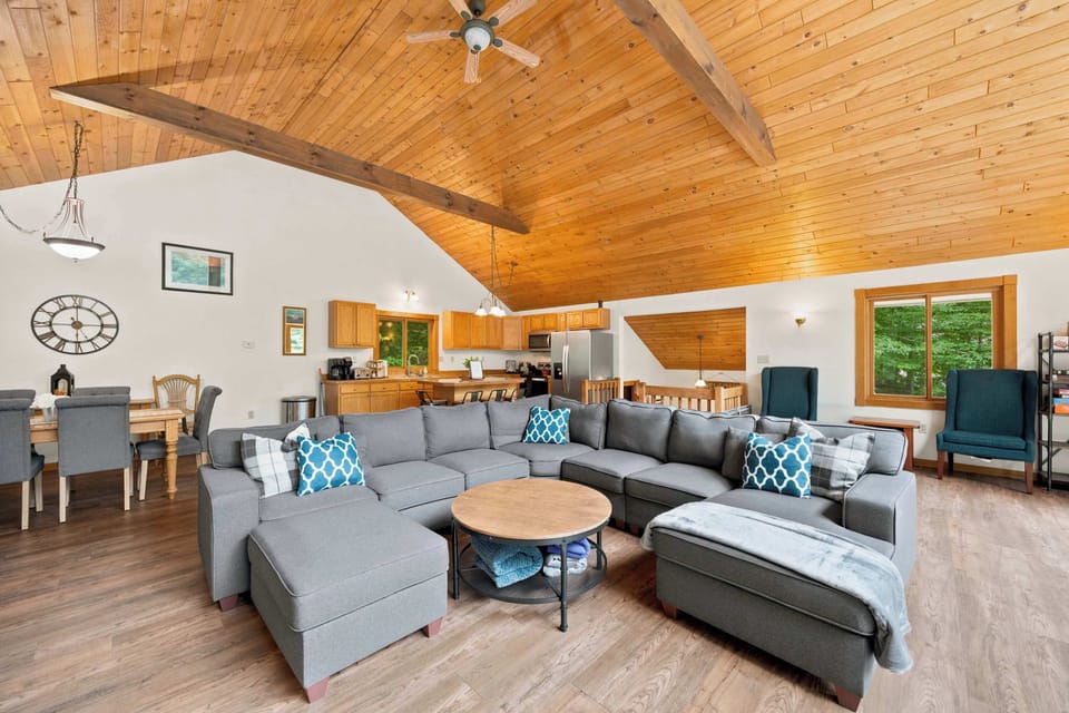 Under the vaulted wood ceiling, the sectional and dining table share one open, light-filled space that flows into the kitchen.
