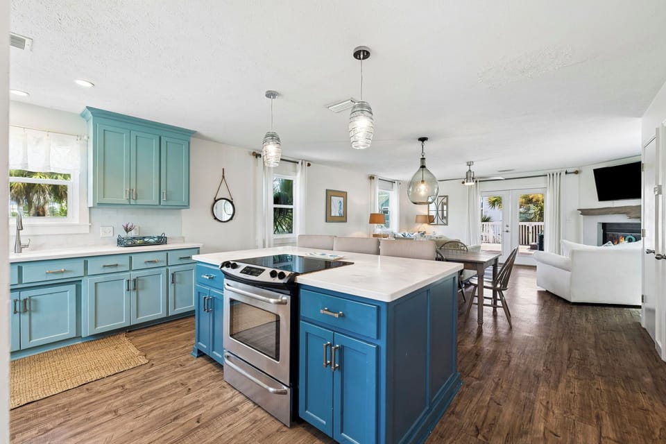 Step into your coastal retreat, where soft blue cabinetry and warm wood floors create an inviting open layout. Cook, gather, and unwind as natural light streams through oversized windows, connecting you to the tropical views beyond.