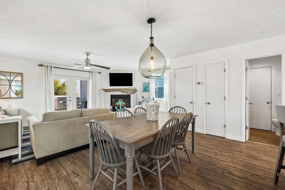 Gather around the rustic dining table in this bright, open living space, where coastal charm meets comfort. Soft natural light pours in through glass doors, inviting you to relax and make memories.