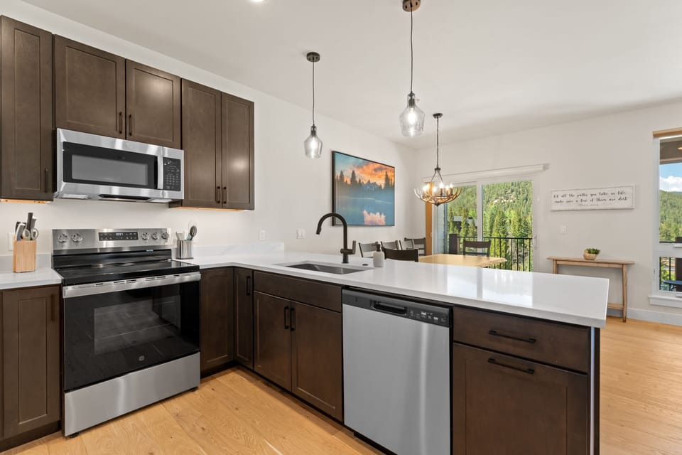 Your modern kitchen awaits, complete with sleek appliances and granite countertops. Pendant lights hang above the island, while natural light streams through the dining area, framing lush greenery beyond.