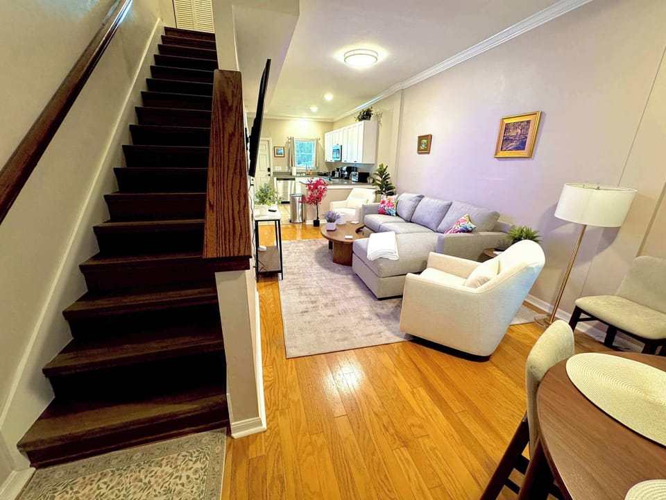 Open-concept, colorful living room with comfortable seating, smart TV (YouTube TV included), and coffee table. Easy access to dining area, kitchen, and stairs to upper story. 
