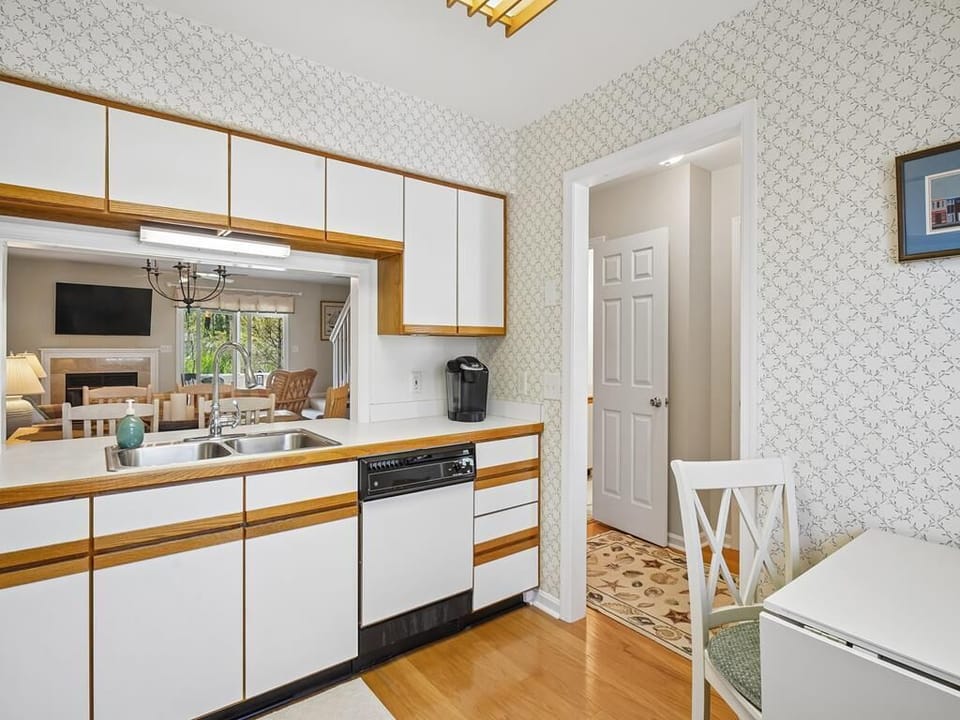 Kitchen with white cabinets, double sink, dishwasher, and coffee maker, open to the living area with Smart TV