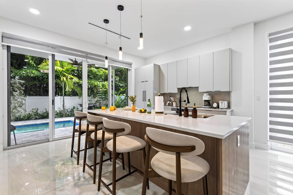 A sleek kitchen island anchors the space beside sunlit pool access.