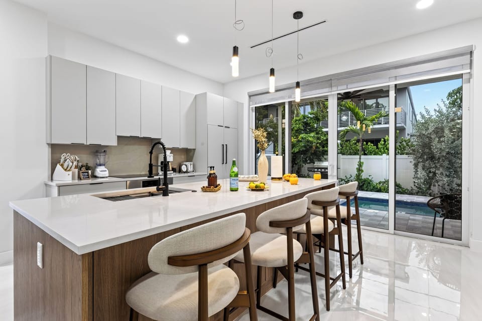 A sleek, sunlit kitchen with a spacious island and bar seating makes gathering effortless.