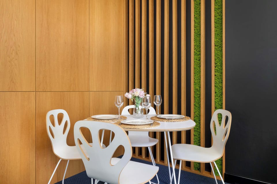 A close-up of a dining nook featuring a white table and four modern chairs. The space is accented by a wall with vertical wooden slats and a solid gray panel.