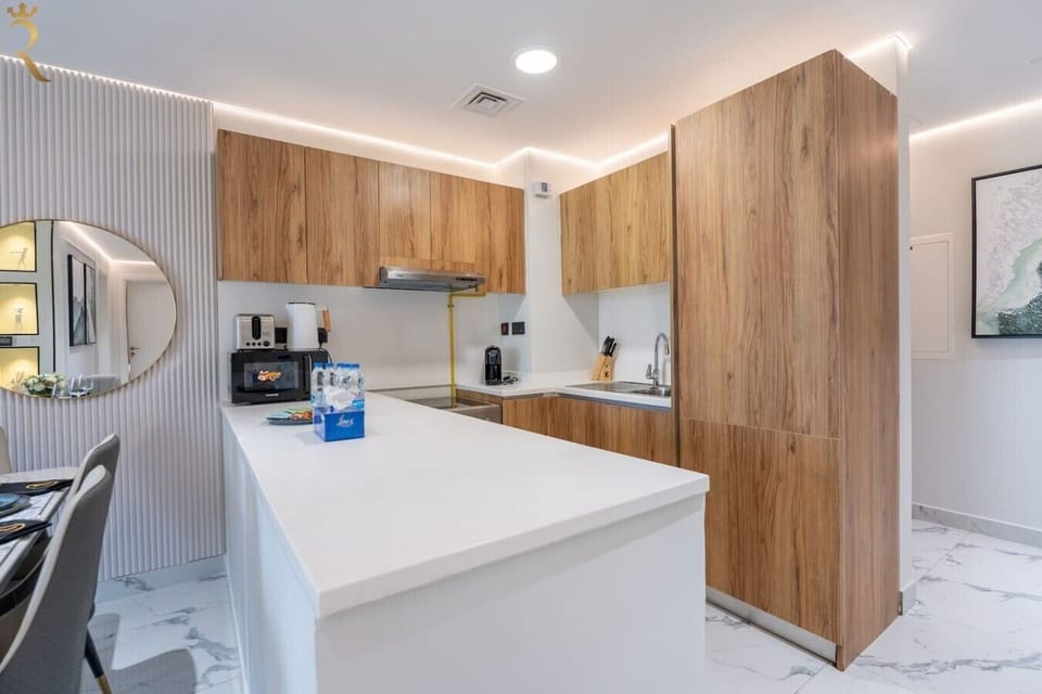 Modern full kitchen with wood-tone cabinetry, quartz countertops, and essential appliances, illuminated by warm under-cabinet lighting.