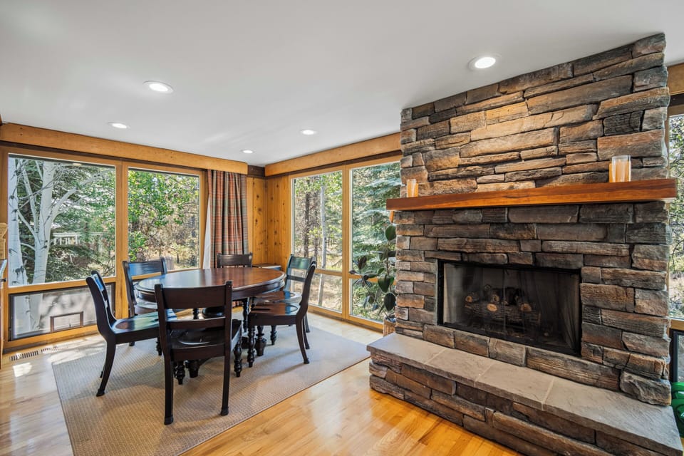 Gather around the rustic stone fireplace and dine with forest views framing your mountain getaway—a warm, inviting space where memorable moments unfold.