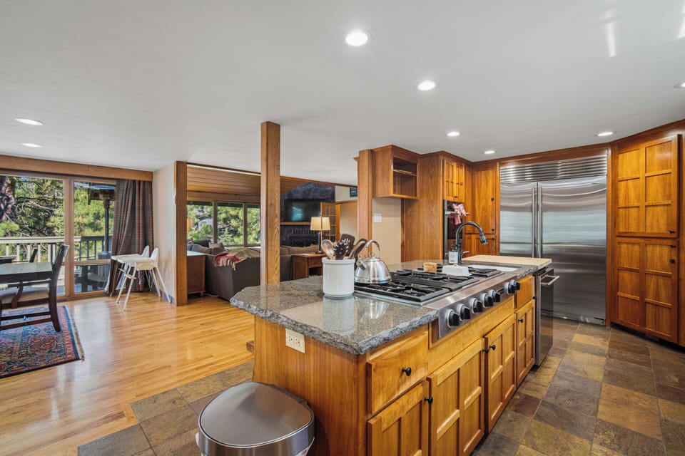 Step into a spacious chef's kitchen with granite countertops, professional-grade appliances, and rich wood cabinetry. Natural light floods through expansive windows framing serene forest views.