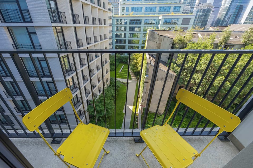 A balcony furnished with vibrant yellow chairs and a small table overlooking the surrounding buildings. It's a pleasant spot for enjoying coffee or relaxing outdoors.