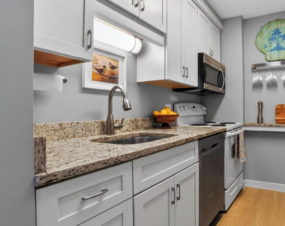 Smooth stone counters and bright cabinetry create a tidy, efficient kitchen perfect for brewing morning coffee. Beachy accents and warm wood floors bring a cheerful coastal energy to this sleek culinary corner.