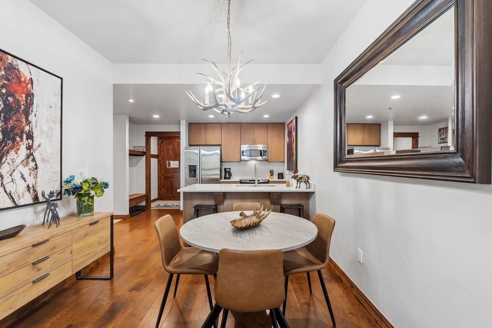 Gather around the dining table where a rustic antler chandelier casts warm light over shared meals. The open kitchen invites you to prepare breakfast together, with modern appliances and abundant counter space making cooking a breeze.