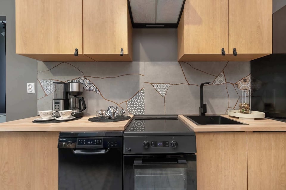 A sleek kitchenette is outfitted with light wooden cabinets and contrasting black appliances. A coffee maker and an electric stove sit neatly on the wooden countertop.