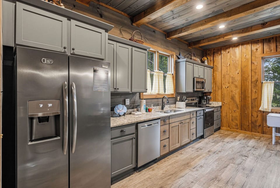 Your fully equipped kitchen features modern appliances, ample counter space, and rustic wood finishes—perfect for preparing meals while enjoying charming natural light through the windows.