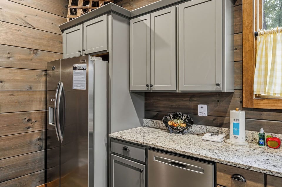 Step into a fully-equipped kitchen blending rustic charm and modern convenience. Gray cabinetry, granite counters, and stainless-steel appliances make meal prep effortless in your home away from home.