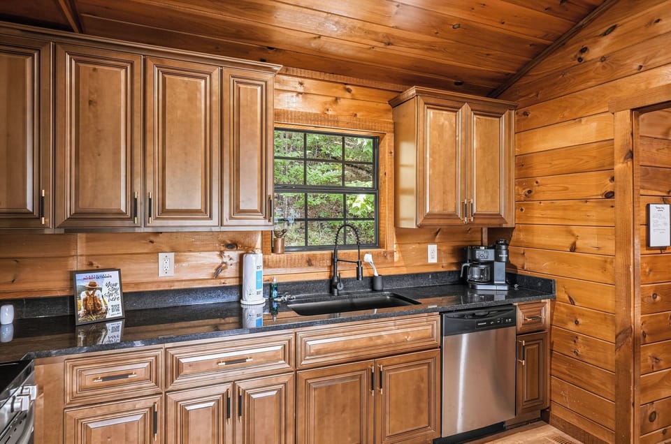 Your fully equipped kitchen features rich wood cabinetry, granite countertops, and modern stainless appliances, all bathed in natural light from the window overlooking the lush outdoors.