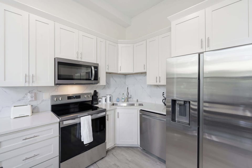 Kitchen | Well-equipped kitchen with white cabinetry, stainless steel range and refrigerator, and tiled backsplash.