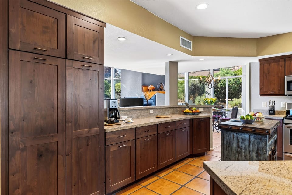A rustic prep island anchors the kitchen, with stainless steel appliances and red-rock glimpses beyond the adjoining dining area.
