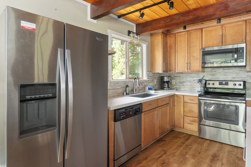 Your fully equipped kitchen features stainless steel appliances, warm wood cabinetry, and natural light streaming through the window—perfect for preparing meals and morning coffee in style.