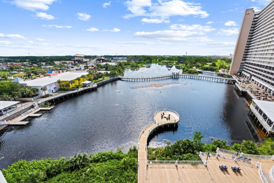 The property overlooks a scenic waterfront area featuring a curved observation pier, wooden boardwalks, and a tranquil lake surrounded by lush greenery and nearby resort buildings.