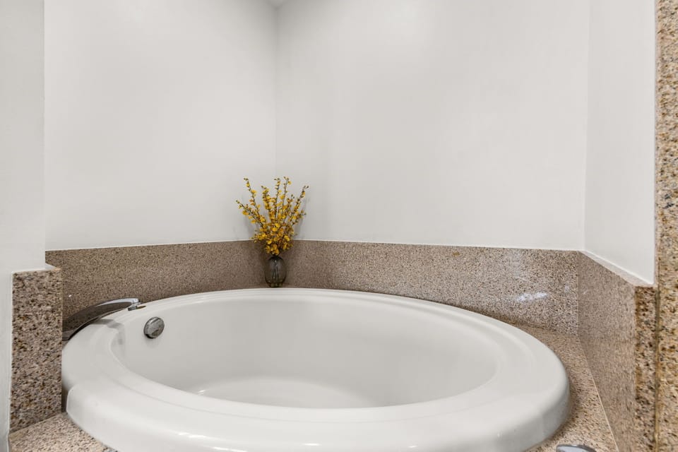 Sink into relaxation in your private soaking tub, framed by warm granite and calming white walls. A simple bouquet of dried flowers adds a cozy, inviting touch.