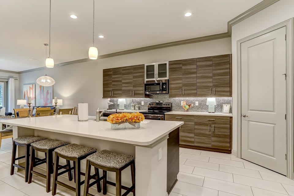 Beautifully designed kitchen featuring sleek wood-grain cabinetry, bright white countertops, and a spacious island. Modern backsplash and warm pendant lighting create the perfect gathering space.