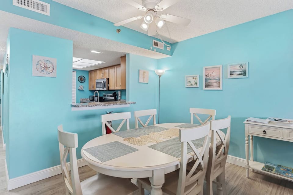 Step into your coastal dining space where turquoise walls and beach-inspired artwork create a breezy, refreshing atmosphere. The white round table awaits your morning coffee or evening meals.