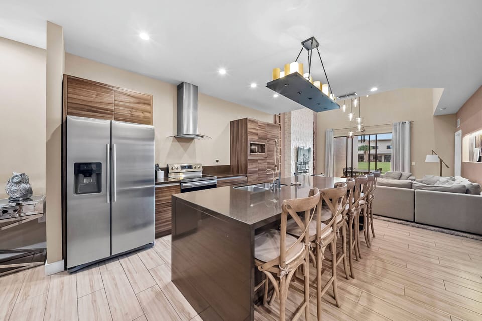 This bright kitchen combines rich wood cabinetry with sleek stainless steel appliances for a warm, contemporary feel. The spacious island with seating is perfect for gatherings, and pendant lighting adds a touch of sophistication.