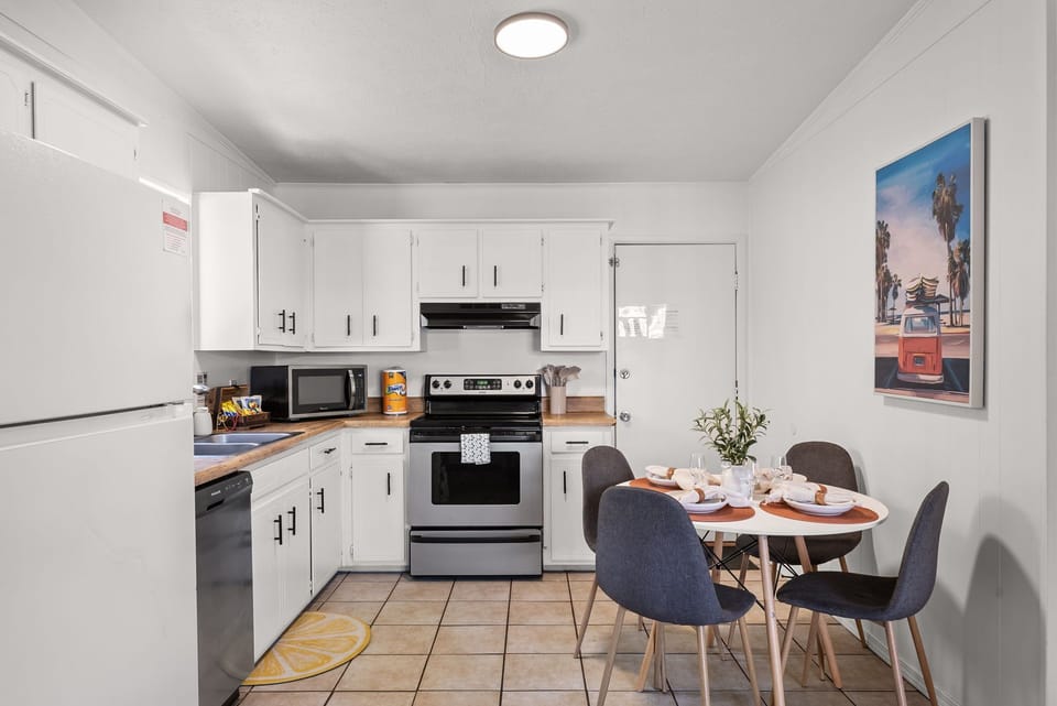 Fully equipped kitchen with white cabinets, modern appliances, and beachy art