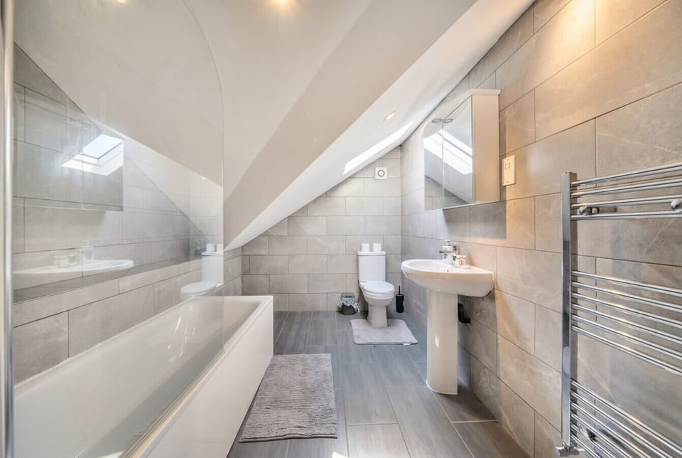 Sleek grey-tiled bathroom with full bath, shower and heated towel rail.