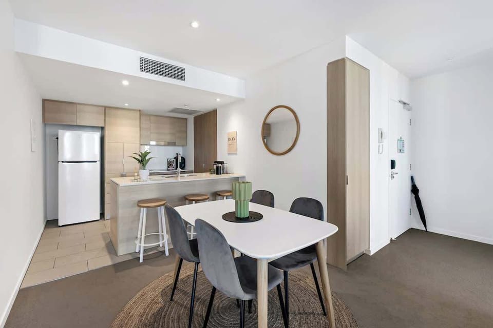 Sleek Urban Living Maximizing space with an open-plan layout, this contemporary apartment features a streamlined timber-look kitchen with breakfast bar seating that flows naturally into a light-filled dining zone anchored by a woven jute rug.