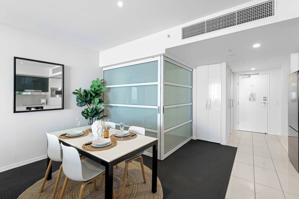 Gather around this modern dining setup featuring a white rectangular table with seating for four, set against a backdrop of sleek frosted glass sliding partition doors and a bright entry hallway.