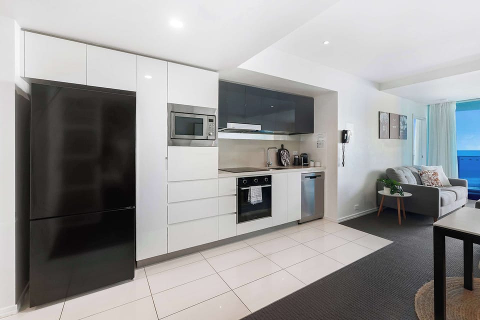 Cook up your favorite meals in this modern kitchen equipped with sleek white cabinetry, a large black refrigerator, integrated appliances, and a built-in microwave, flowing seamlessly into the open living space.
